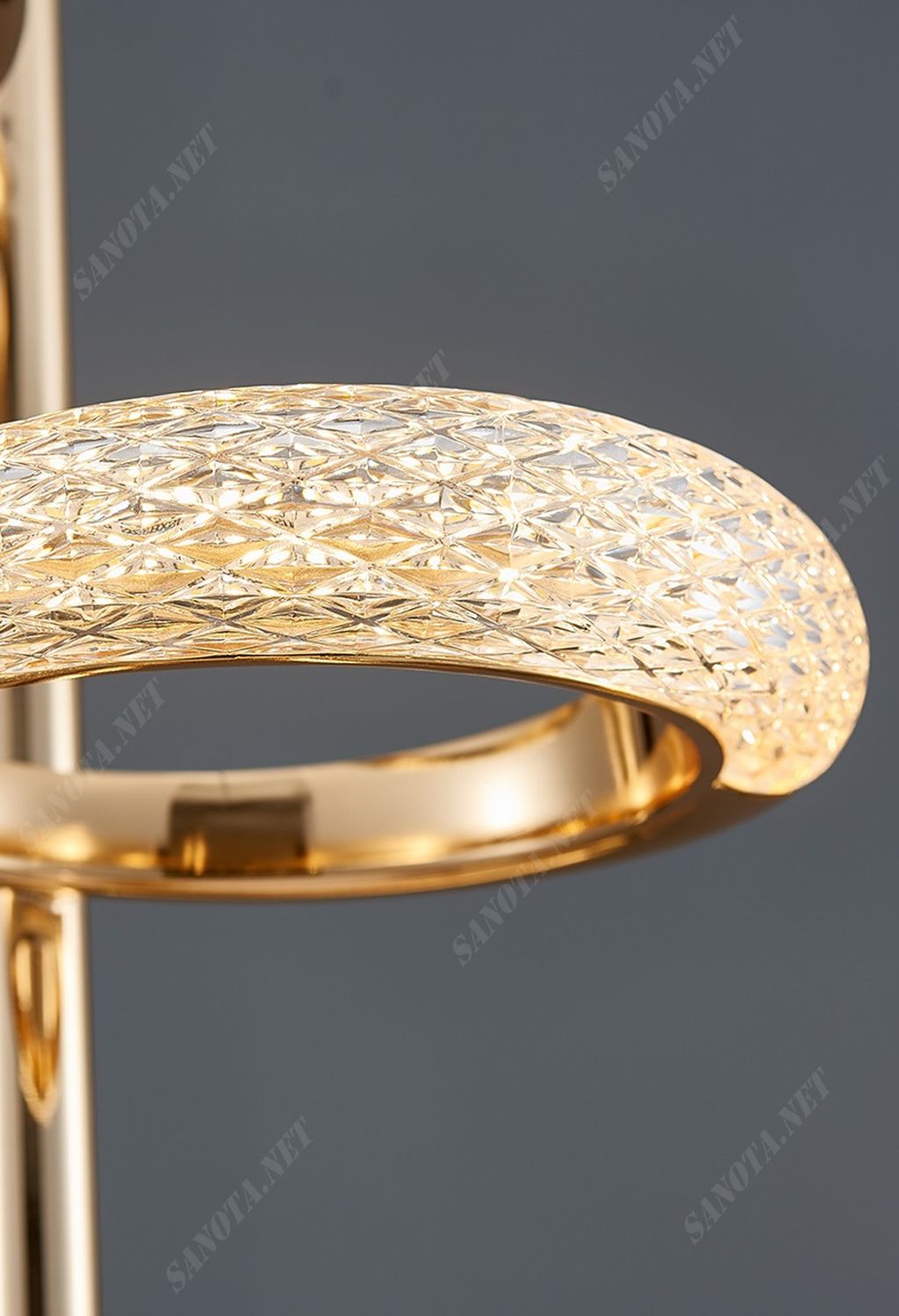 Một chiếc đèn thả trần, kiệt tác vẻ đẹp từng đường nét, hình dạng mềm mại như một chiếc nhẫn pha lê màu vàng, đính kèm với sự lấp lánh và sang trọng không thể nhầm lẫn. Mỗi pha lê mềm mại, tỏa sáng trong ánh đèn, tạo nên một vẻ đẹp lộng lẫy và đặc biệt khi ánh sáng đi qua, tạo ra một nguồn ánh sáng độc đáo nhưng vẫn dịu dàng và tinh tế. Khi ánh sáng chiếu qua, từng viên pha lê như những ngọc quý, phản chiếu và tạo ra một loạt các tia sáng mềm mại, làm nổi bật vẻ đẹp tinh tế và sang trọng của đèn. Mỗi chi tiết trên chiếc đèn như những viên ngọc quý vẫn lấp lánh dưới ánh sáng, tạo cảm giác bừng sáng nhưng vẫn giữ được vẻ dịu dàng, tạo không gian ấm áp và thanh lịch.