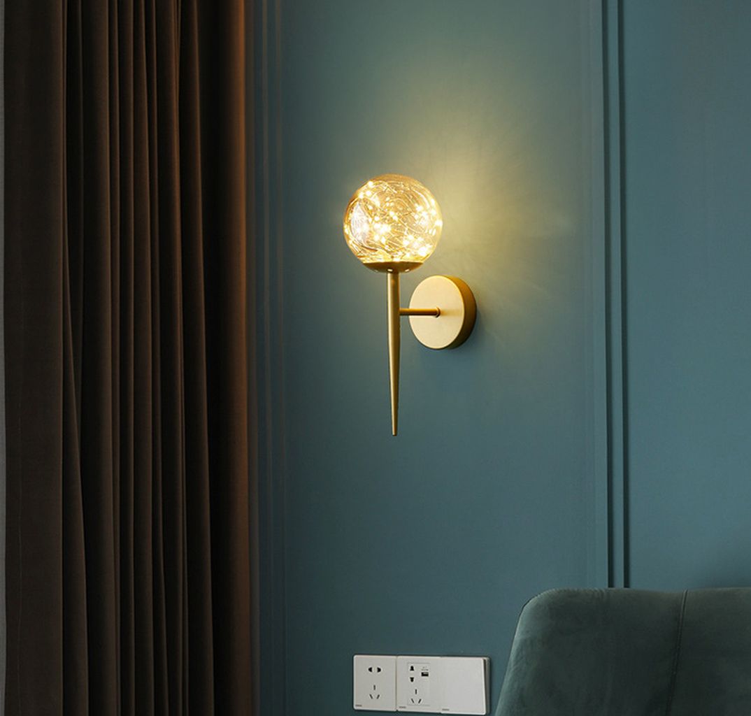 Thân đèn được làm từ một thanh hợp kim mạ vàng quý phái. Được cố định mạnh mẽ bởi một đế đèn chắc chắn trên tường. Điểm độc đáo của chiếc đèn nằm ở bóng đèn chao thuỷ tinh. Hình dạng như một viên đá cẩm thạch, tạo điểm nhấn thu hút cho toàn bộ thiết kế. Sự kết hợp của hợp kim mạ vàng và chất liệu chao thuỷ tinh tạo nên một kiệt tác nghệ thuật. Giống như một cây quyền trượng độc đáo. Khi bật ánh sáng, bóng đèn LED phát ra một ánh sáng ấm áp, dịu dàng.