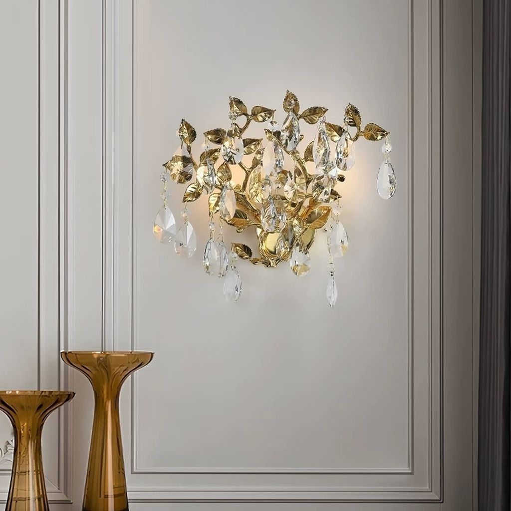 Đèn tường hoa pha lê được chế tác với khung mạ vàng ánh kim nổi bật, uốn lượn thành từng nhánh lá mềm mại. Kết hợp khéo léo cùng pha lê cao cấp cắt giác hoàn hảo. Ánh sáng lan tỏa nhẹ nhàng phản chiếu qua từng giọt pha lê. Tạo nên hiệu ứng lung linh, quyến rũ, đầy thu hút. Kiểu dáng đèn như một nhành cây vàng óng ánh đơm hoa kết trái. Mang ý nghĩa phồn vinh và thịnh vượng cho gia chủ.