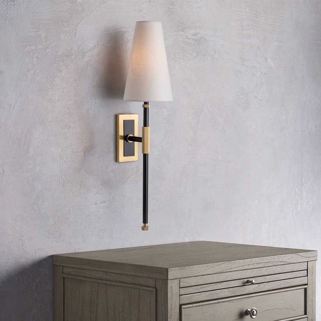 Đèn tường phong cách Bắc Âu gây ấn tượng ngay từ cái nhìn đầu tiên. Với thiết kế thân đèn thẳng đứng kết hợp cùng đế mạ vàng cao cấp. Tạo nên vẻ đẹp thanh thoát mà đầy đẳng cấp. Chụp đèn vải trắng hình nón mềm mại giúp ánh sáng tỏa đều, ấm áp. Lý tưởng để tạo nên không gian thư giãn nhẹ nhàng trong phòng ngủ, hành lang hay khu vực tiếp khách.