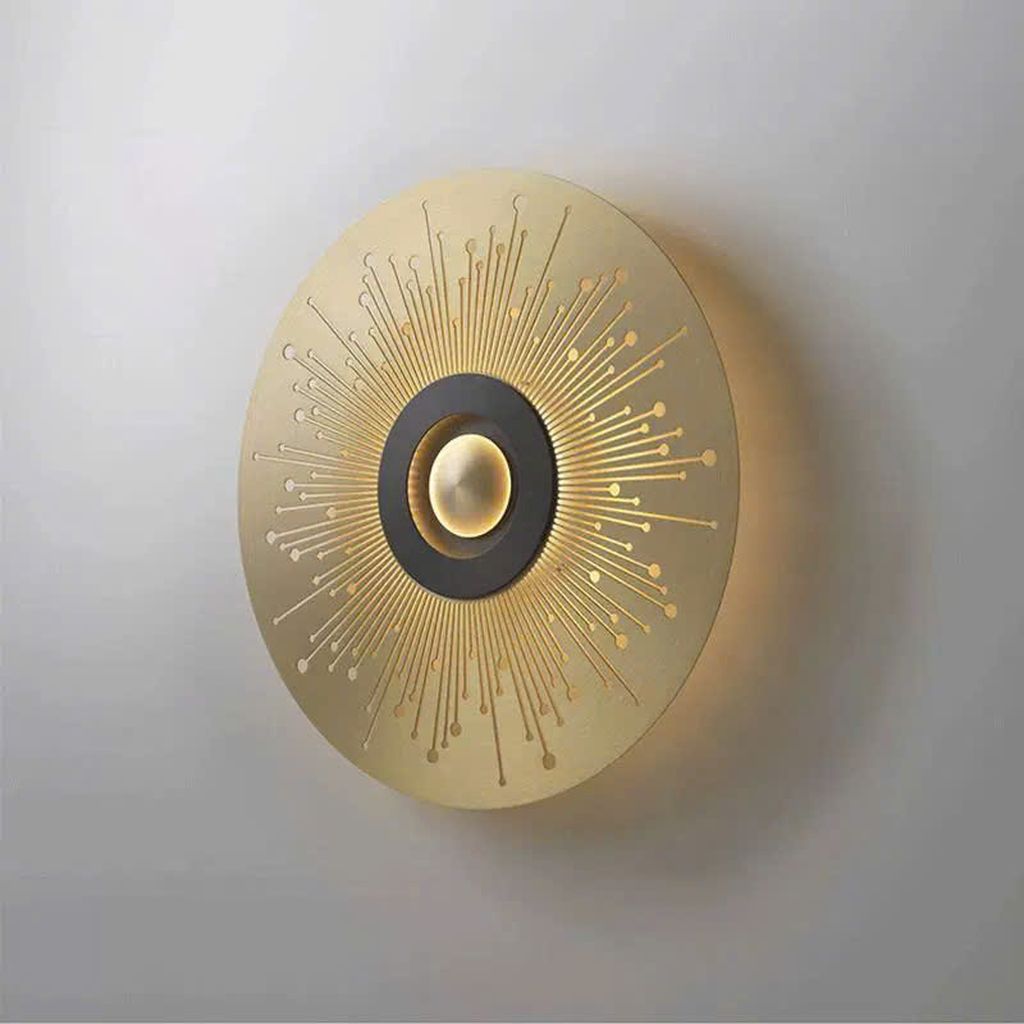Đèn tường nghệ thuật lấy cảm hứng từ hình ảnh mặt trời tỏa sáng, thiết kế đèn mang hình dáng đĩa tròn mạ vàng với các tia sáng lan tỏa đều xung quanh tâm điểm. Ánh sáng LED dịu nhẹ được tích hợp khéo léo sau lớp kim loại, tạo nên hiệu ứng ánh sáng phản chiếu đầy mê hoặc. Khiến mỗi lần bật đèn là một lần không gian bừng sáng đầy nghệ thuật. Vẻ đẹp của đèn tường không chỉ nằm ở chất liệu kim loại cao cấp được xử lý tỉ mỉ mà còn ở cách ánh sáng lan tỏa theo những họa tiết đối xứng. Tạo cảm giác như một mặt trời thu nhỏ đang tỏa nắng lên bức tường nhà bạn.