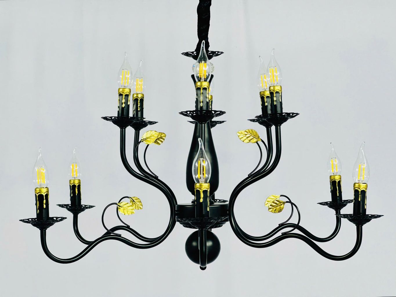 Đèn chùm cổ điển gây ấn tượng mạnh với khung sắt sơn tĩnh điện màu đen bóng sang trọng. Kết hợp với chi tiết lá vàng kim loại tạo điểm nhấn độc đáo và đầy nghệ thuật. Những tay đèn được uốn cong mềm mại như những nhánh cây vươn mình. Mang đến cảm giác nhẹ nhàng mà vẫn vững chãi. Mỗi ngọn đèn LED giả nến được bố trí khéo léo, ánh sáng vàng ấm áp giúp tạo nên không gian ấm cúng, gần gũi mà vẫn không kém phần quý phái.