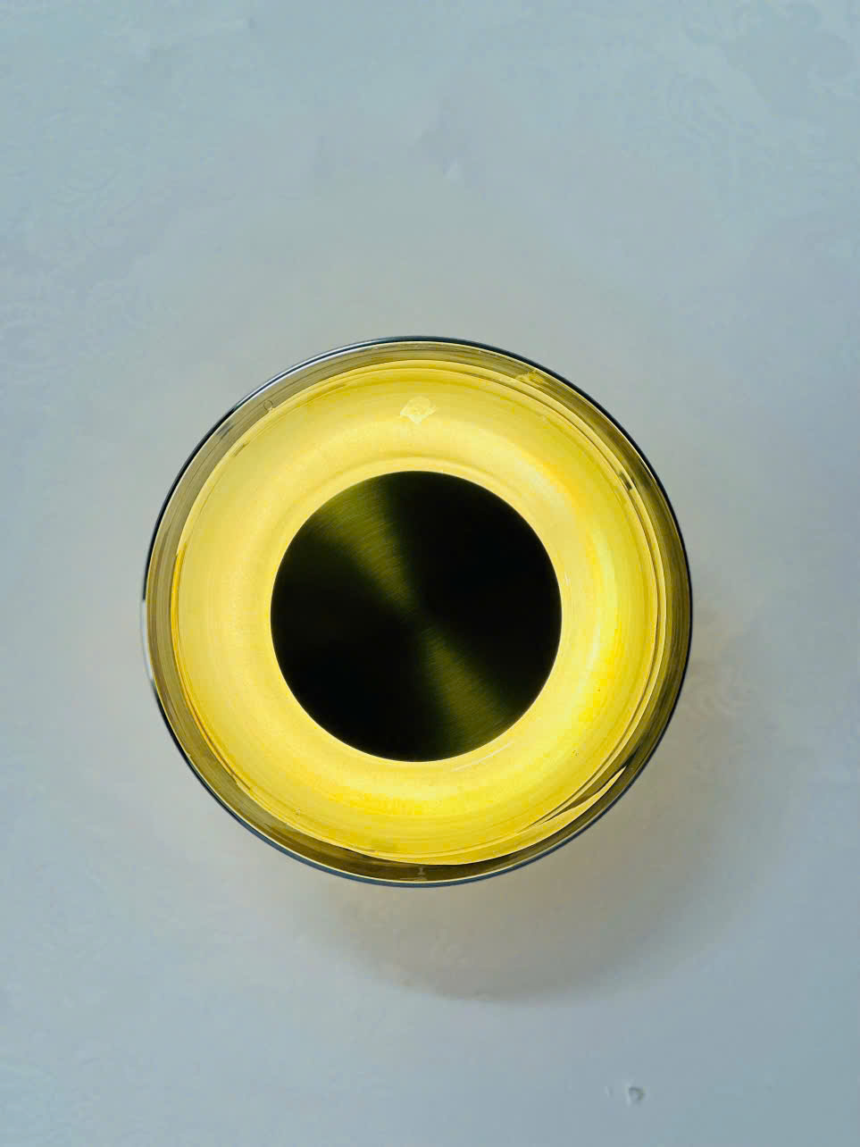 Đèn tường thuỷ tinh được thiết kế với phần chao trong suốt tinh tế, bao quanh lõi ánh sáng LED vàng ấm tạo nên hiệu ứng thị giác nổi bật, vừa hiện đại vừa ấm cúng. Nhìn từ mặt trước, chiếc đèn mang hình dáng vòng tròn đồng tâm hoàn hảo, tạo cảm giác hài hòa và nhẹ nhàng, như một "vầng hào quang" thu nhỏ trên bức tường. Lớp kim loại ánh đồng ở tâm đèn không chỉ tăng độ phản chiếu ánh sáng mà còn mang đến sự sang trọng khó cưỡng.