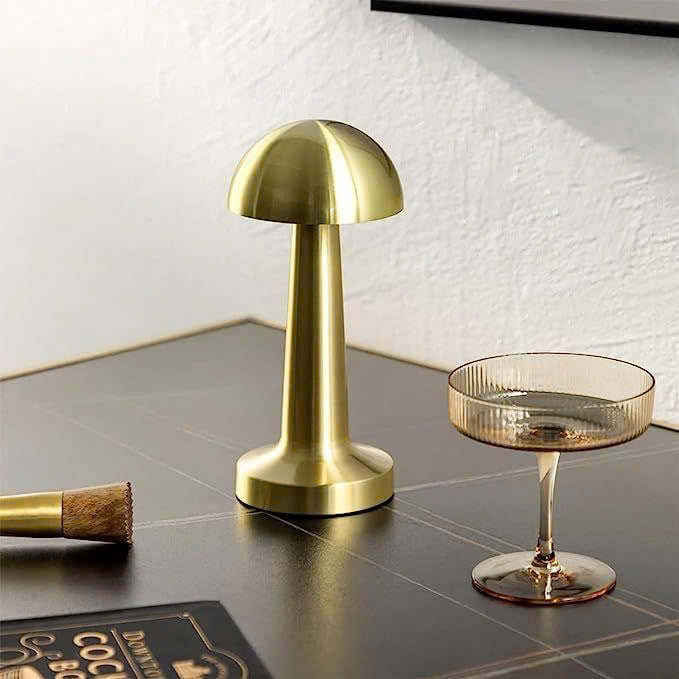 Đèn để bàn mạ vang lấy cảm hứng từ hình dáng cây nấm nhỏ xinh. Đèn để bàn nổi bật với thiết kế tối giản, gọn gàng mà vẫn tinh tế đến từng đường nét. Toàn bộ thân đèn được phủ lớp mạ vàng bóng mượt, phản chiếu ánh sáng nhẹ nhàng. Tạo cảm giác ấm áp và sang trọng cho căn phòng.